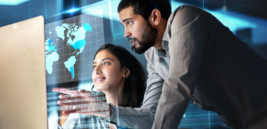 Two teammates collaborating in an office, looking at a monitor with a transparent overlay of a map on the display